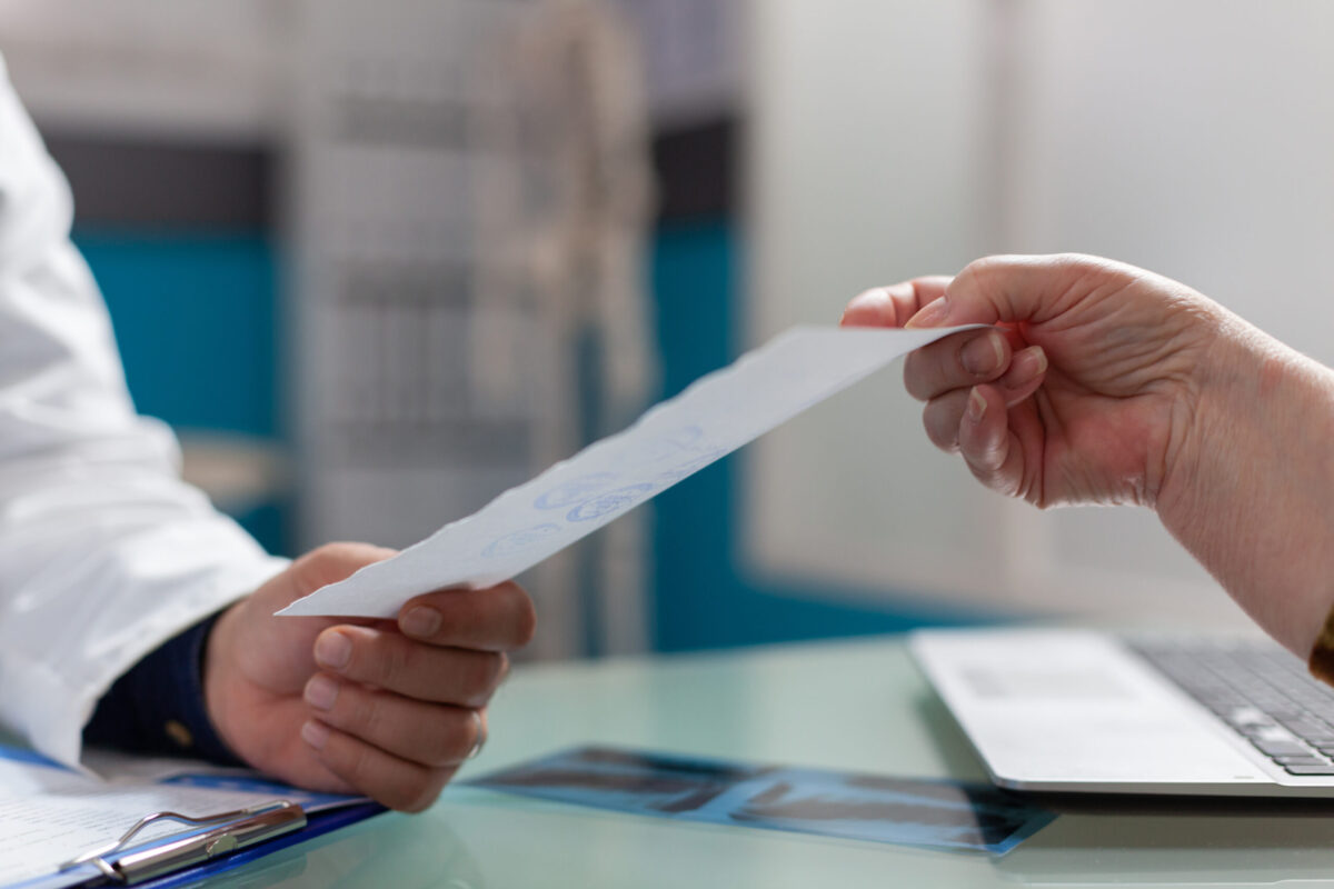 Physician giving prescription document to patient in cabinet, after medical consultation. Medic holding checkup report to give treatment to retired person in health care office. Close up